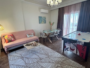 A living room with a sofa, coffee table, dining table, chairs, a chandelier, and a foosball table. - Coral Urbanite (Rodos)