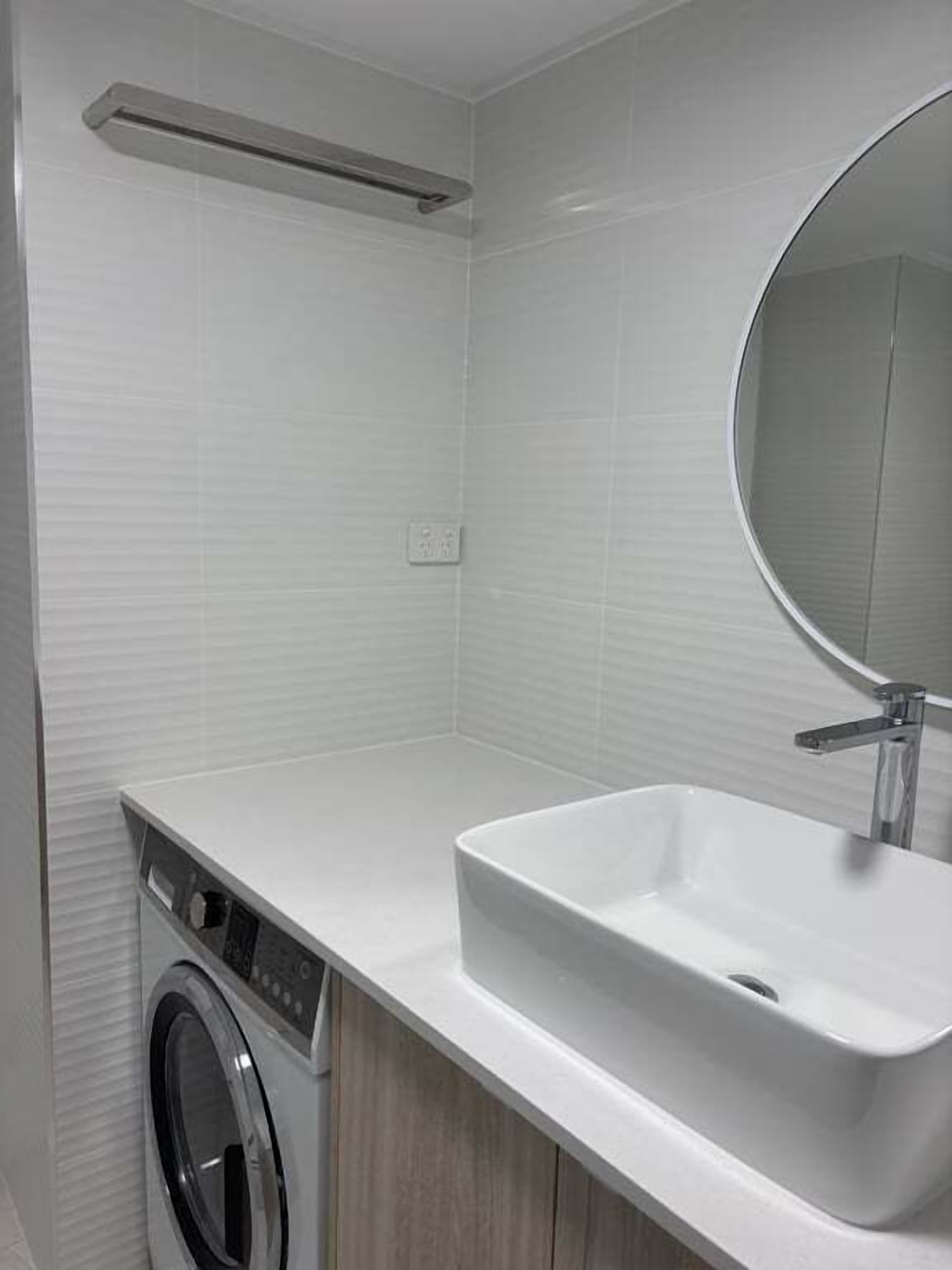 A modern bathroom with a built-in washing machine, a sink, and a mirror.