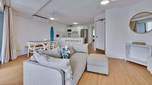 A modern living room with a sofa, ottoman, and a dining area with a table and chairs. - 7 Coral Seas 35-37 Sixth Avenue (Maroochydore)