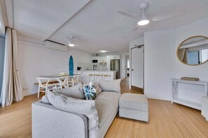 Ein modernes Wohnzimmer mit einer Couch, einem Hocker und einem Essbereich mit Tisch und Stühlen.