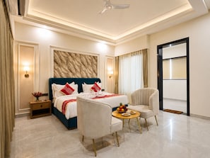 Habitación de hotel con cama, dos sillones, una mesita con fruta, una mesita de noche y vistas al exterior.