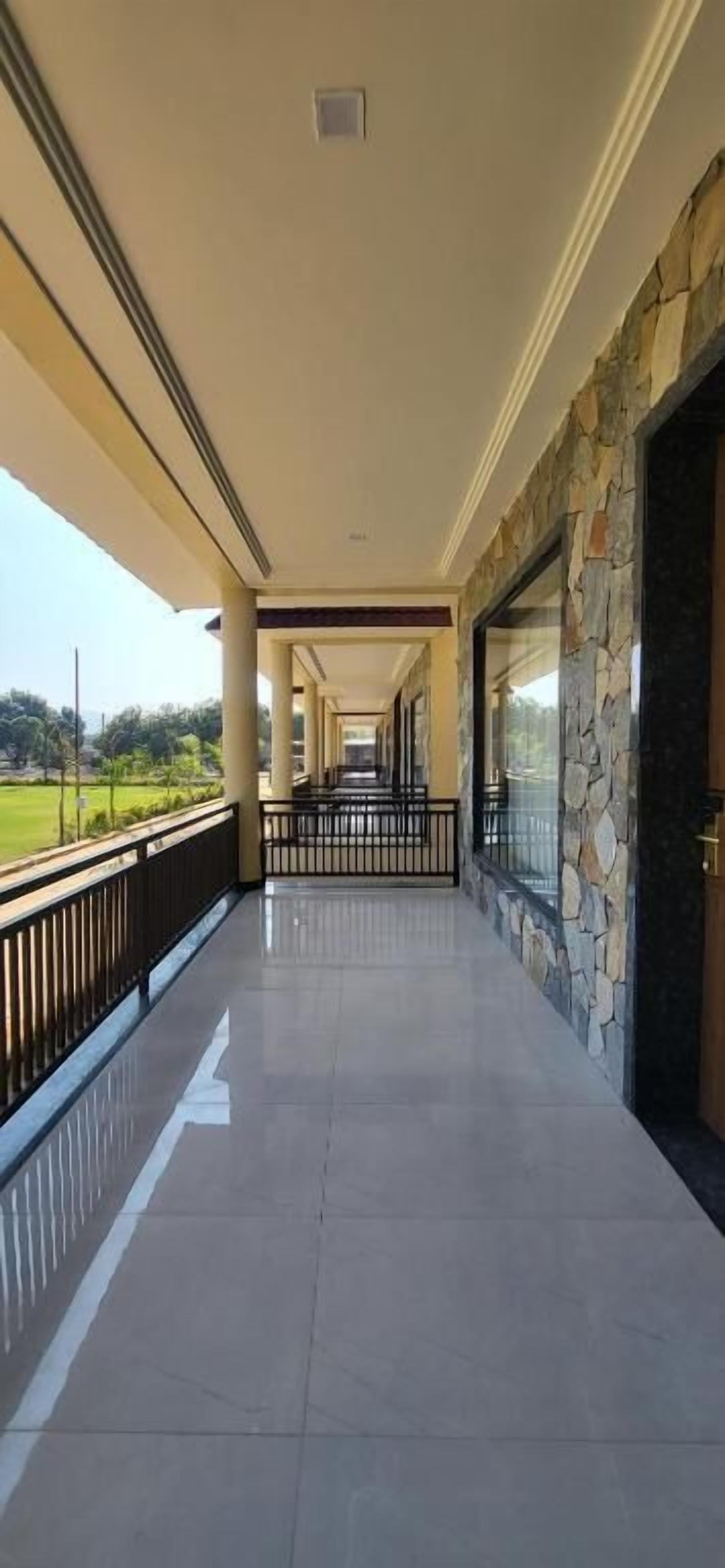 A covered corridor with stone walls, a metal railing, and a view of greenery.