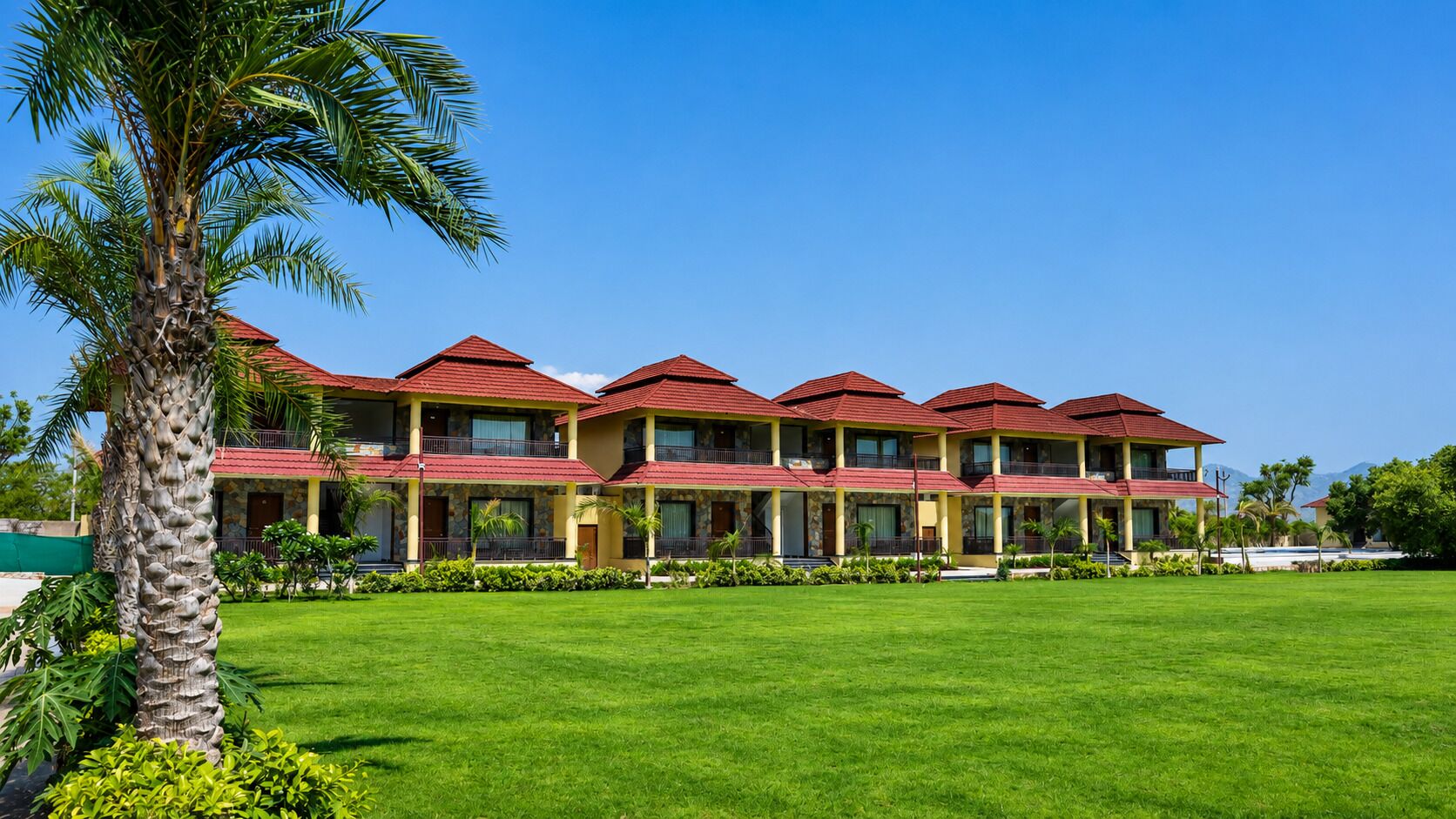 A hotel with multiple red-roofed buildings, a well-maintained lawn, and a palm tree.