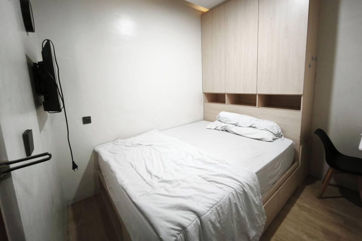 A bedroom with a bed, a wardrobe, a desk, and a chair.