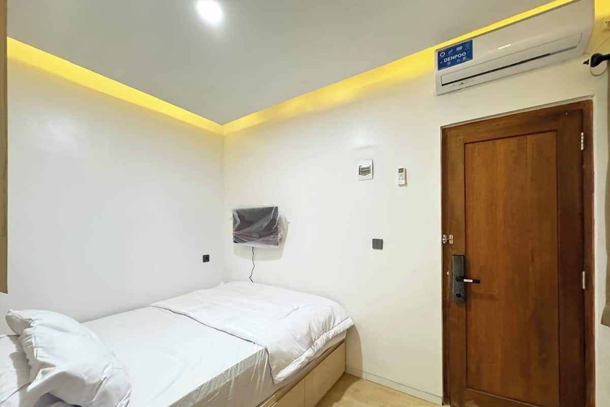 A bedroom with a bed, a wooden door, an air conditioning unit, and a wall-mounted television.