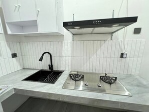 A kitchen with a sink, two gas stoves, a black range hood, white cabinets, and a tiled backsplash. - Malano Residence (Denpasar)