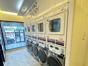 A laundry facility with multiple washing machines, each labeled with capacity and brand. - Malano Residence (Denpasar)