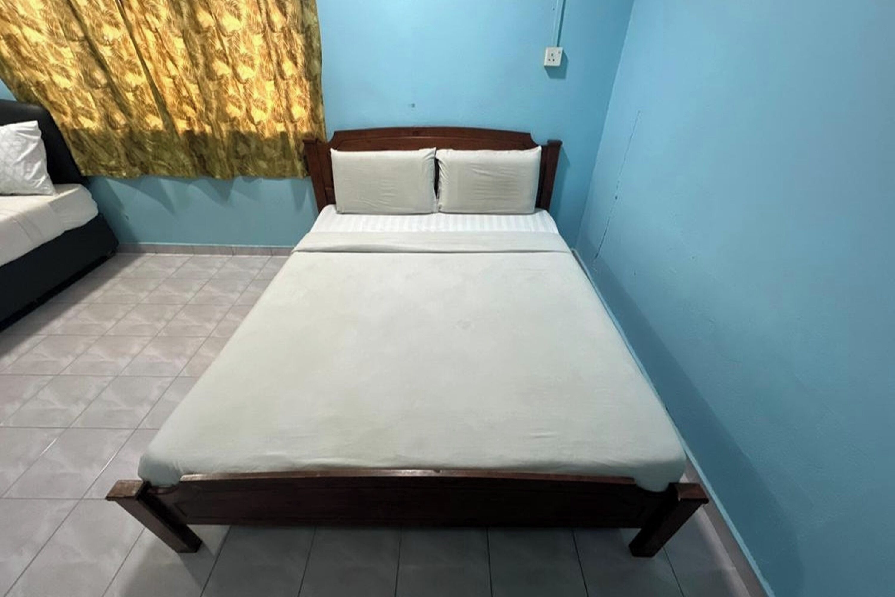 Una cama individual con estructura de madera, ropa de cama blanca y una cortina cubriendo parcialmente una ventana.