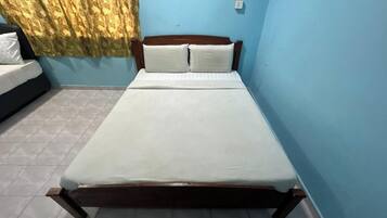 Una cama individual con estructura de madera, ropa de cama blanca y una cortina cubriendo parcialmente una ventana.