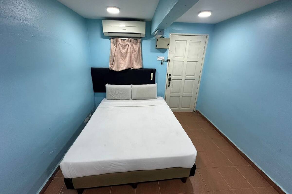 A bedroom with a bed, an air conditioning unit, a door, and a curtain.