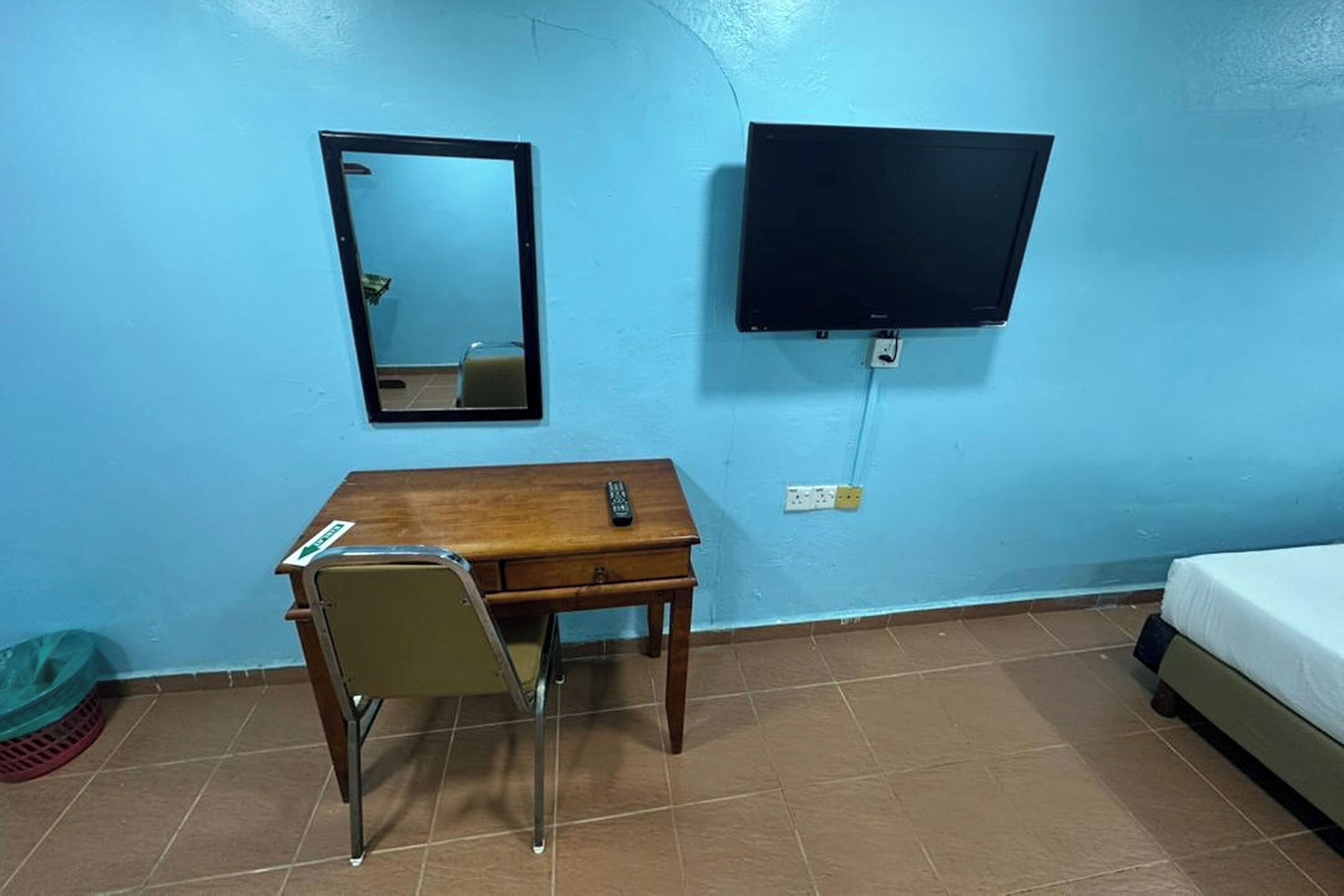 A room with a wooden desk, a chair, a television mounted on the wall, and a bed.