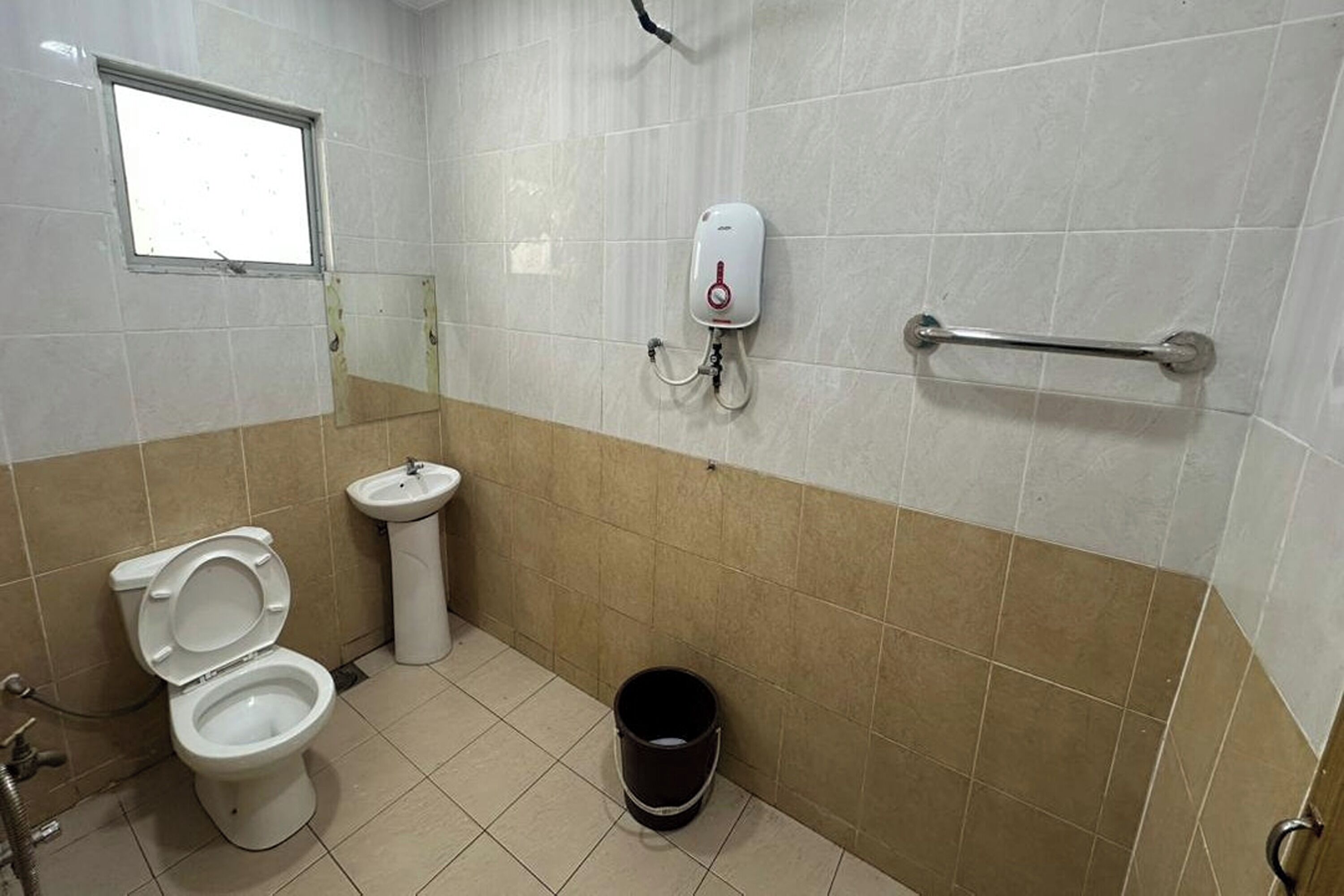 Un baño con inodoro, lavamanos, secamanos, barra de apoyo y ventana.