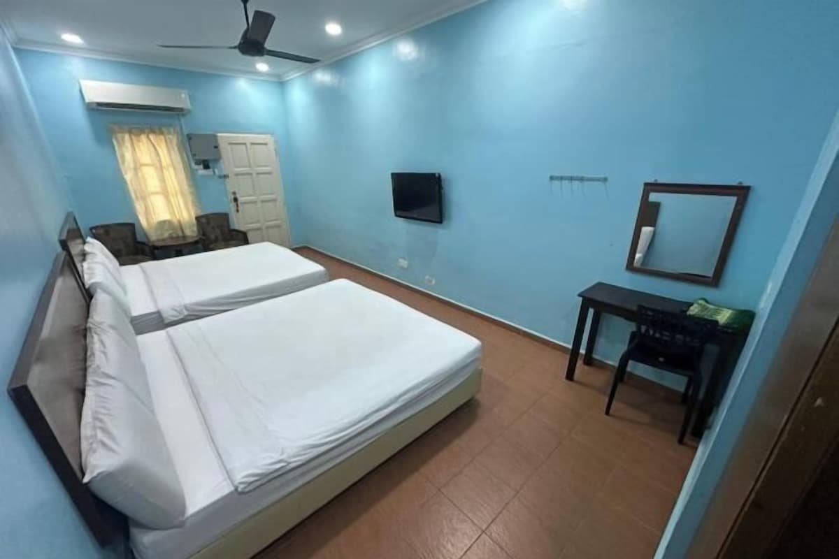 Habitación de hotel con cama, escritorio, silla, televisor y ventilador de techo.