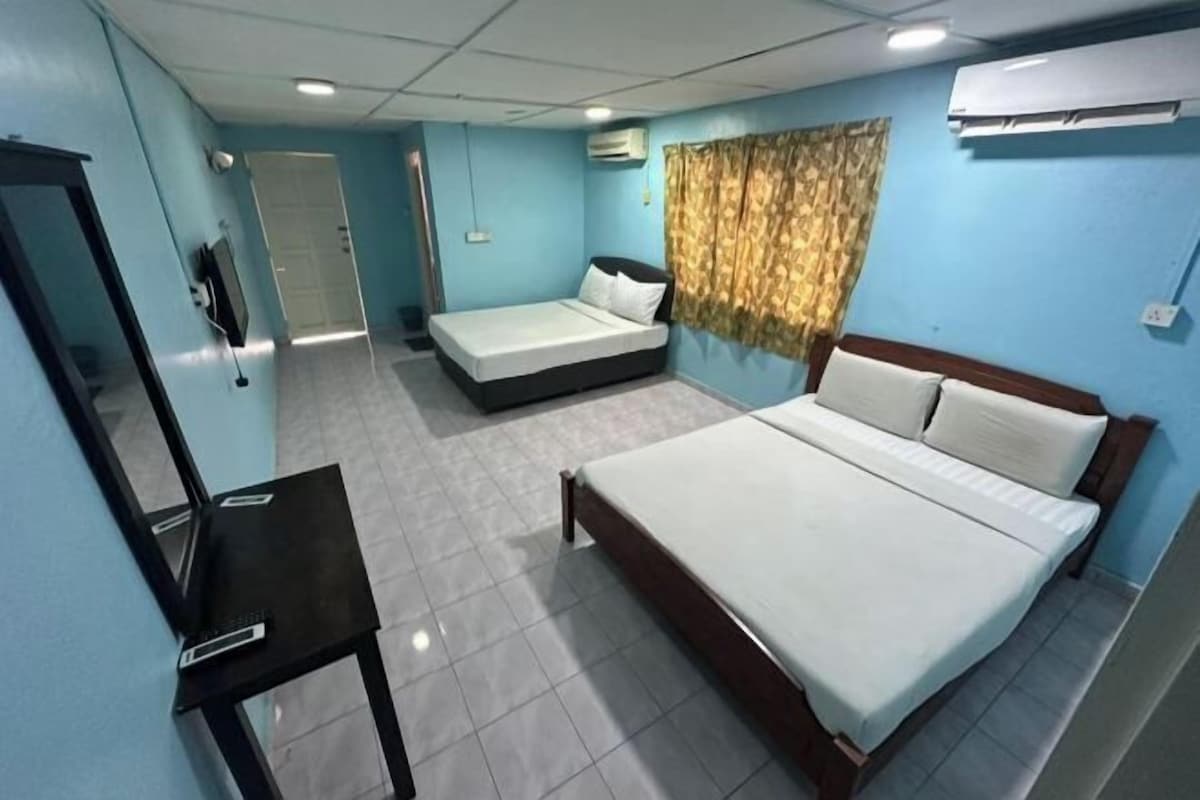 Habitación de hotel con una cama grande, una cama más pequeña, un escritorio y un espejo.