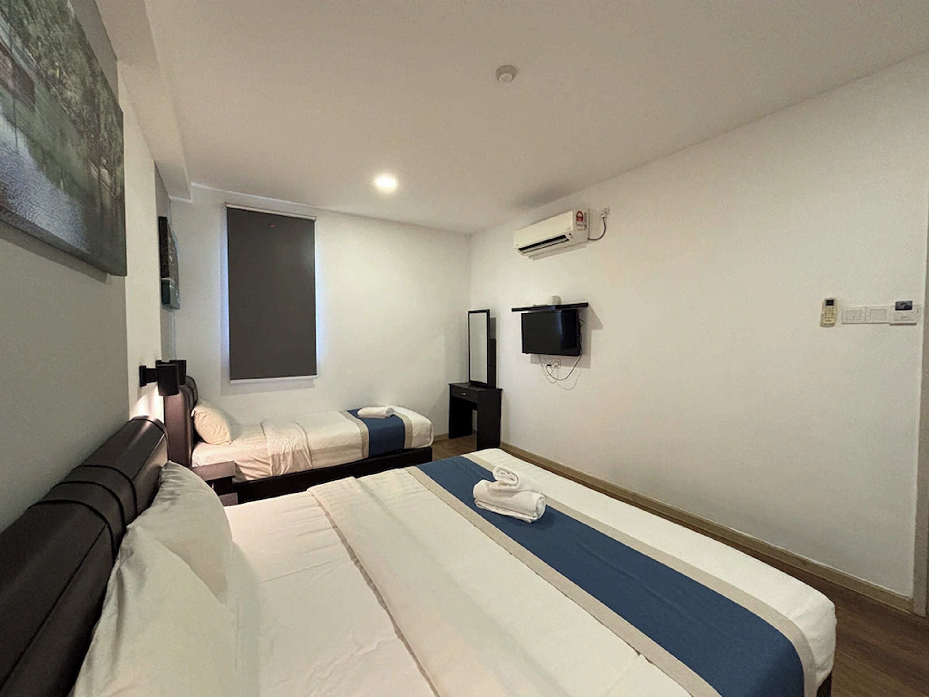 Ein Hotelzimmer mit zwei Betten, einem Flachbildfernseher, einer Klimaanlage und einem großen Fenster.