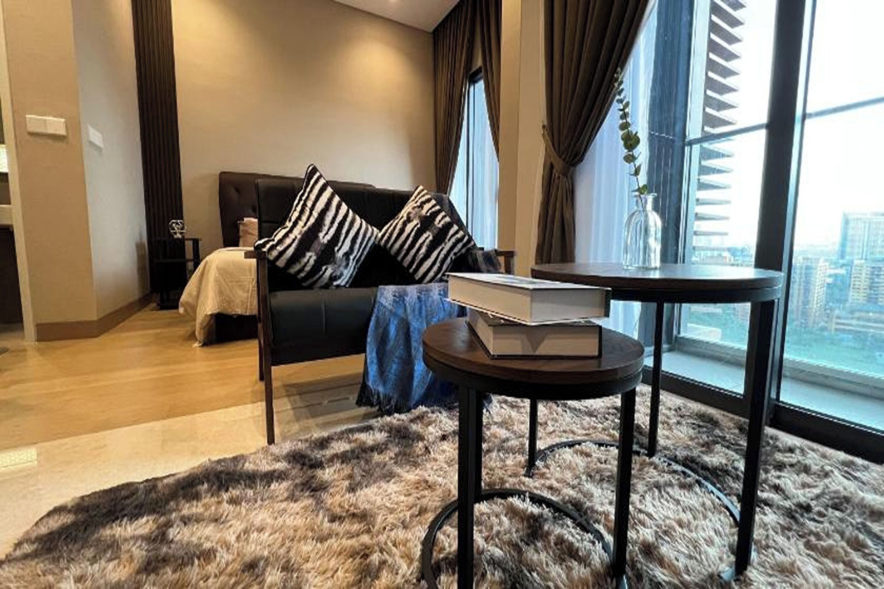 A modern living room with a sofa, a round table, and a large window with a view of the city.