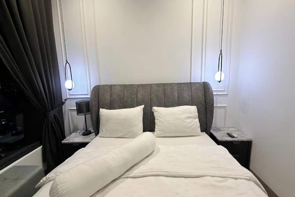 Una cama bien hecha con sábanas blancas, dos mesitas de noche con lámparas y un ventanal con cortinas.