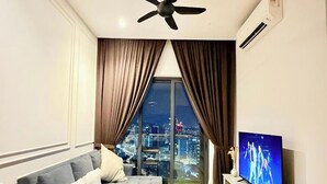 A modern living room with a sofa, a coffee table, a TV, and a city view through large windows. - Lucentia Residence Bukit Bintang Lalaportbbcc By Vellora (Kuala Lumpur)