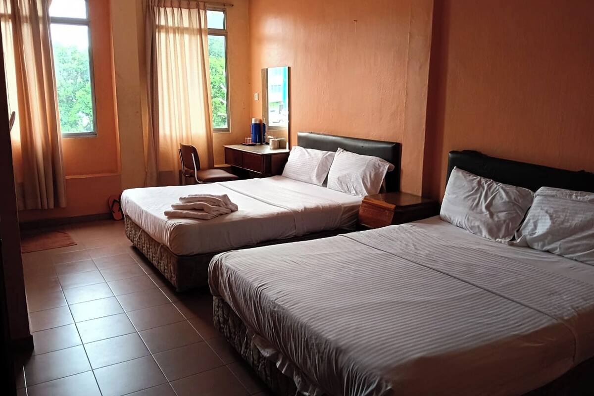 A hotel room with two beds, a desk, a chair, and a window with curtains.