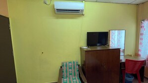 Una habitación con una pared amarilla, un armario de madera, un televisor encima, una mesita, una silla roja y un banco estampado.
