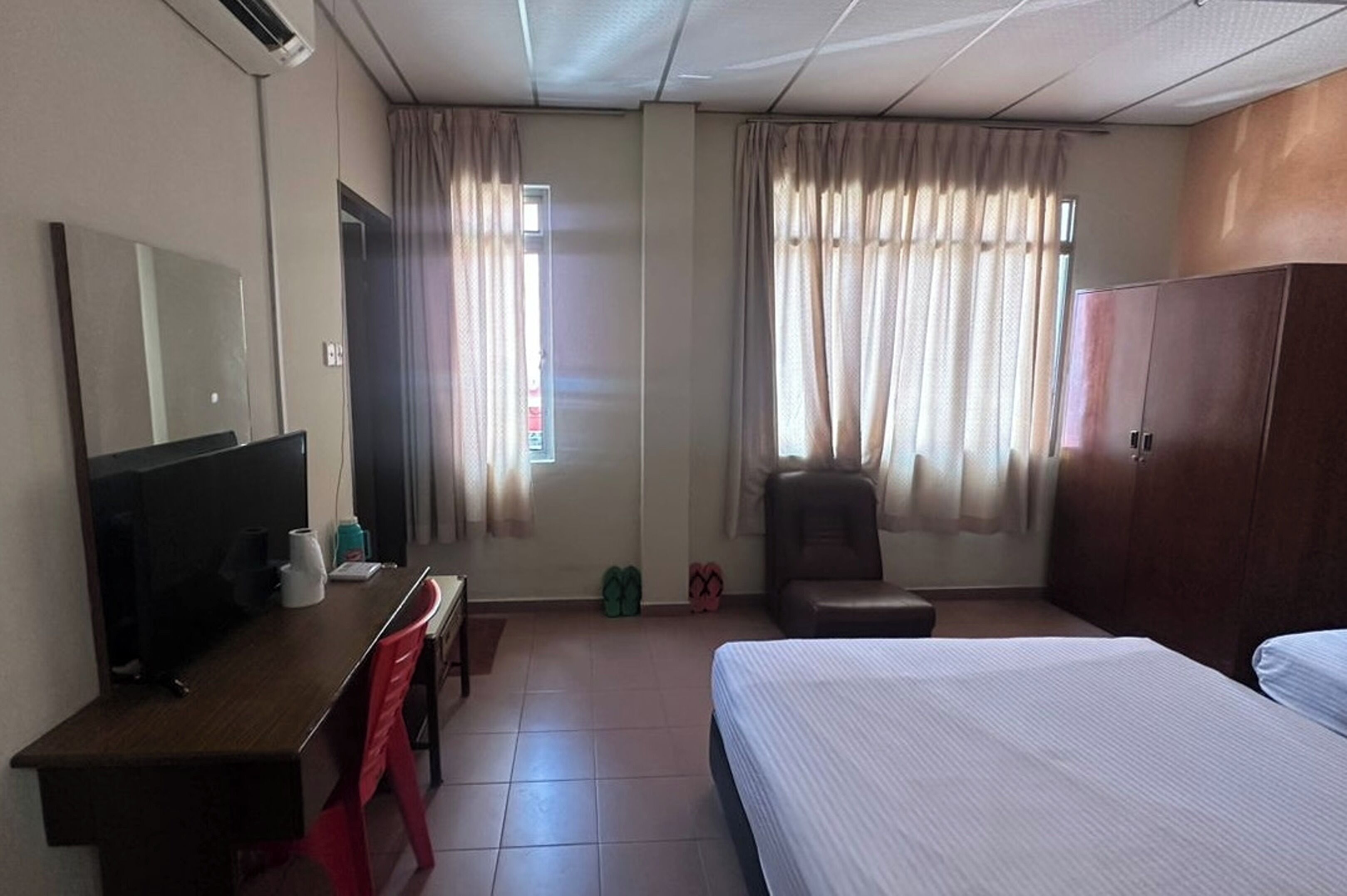 Una habitación de hotel con una cama, un escritorio con silla, un armario y cortinas.