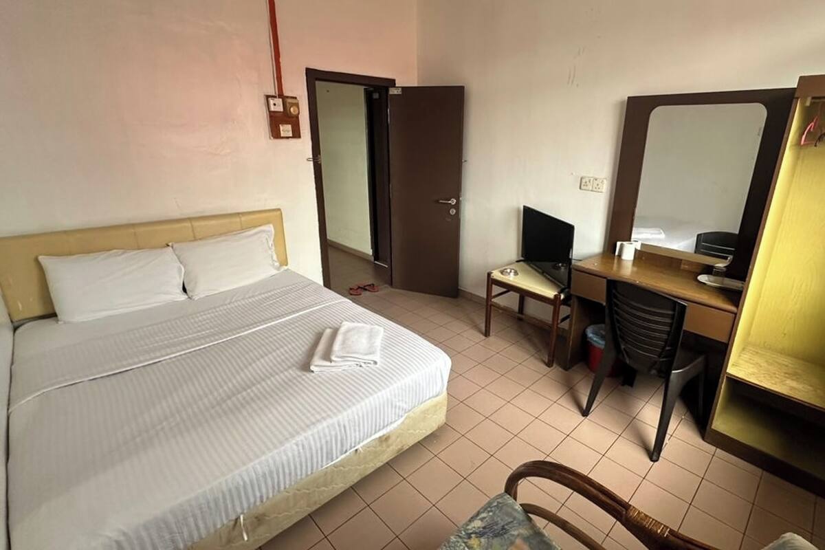 A hotel room with a bed, a desk, a chair, a computer, and a mirror.