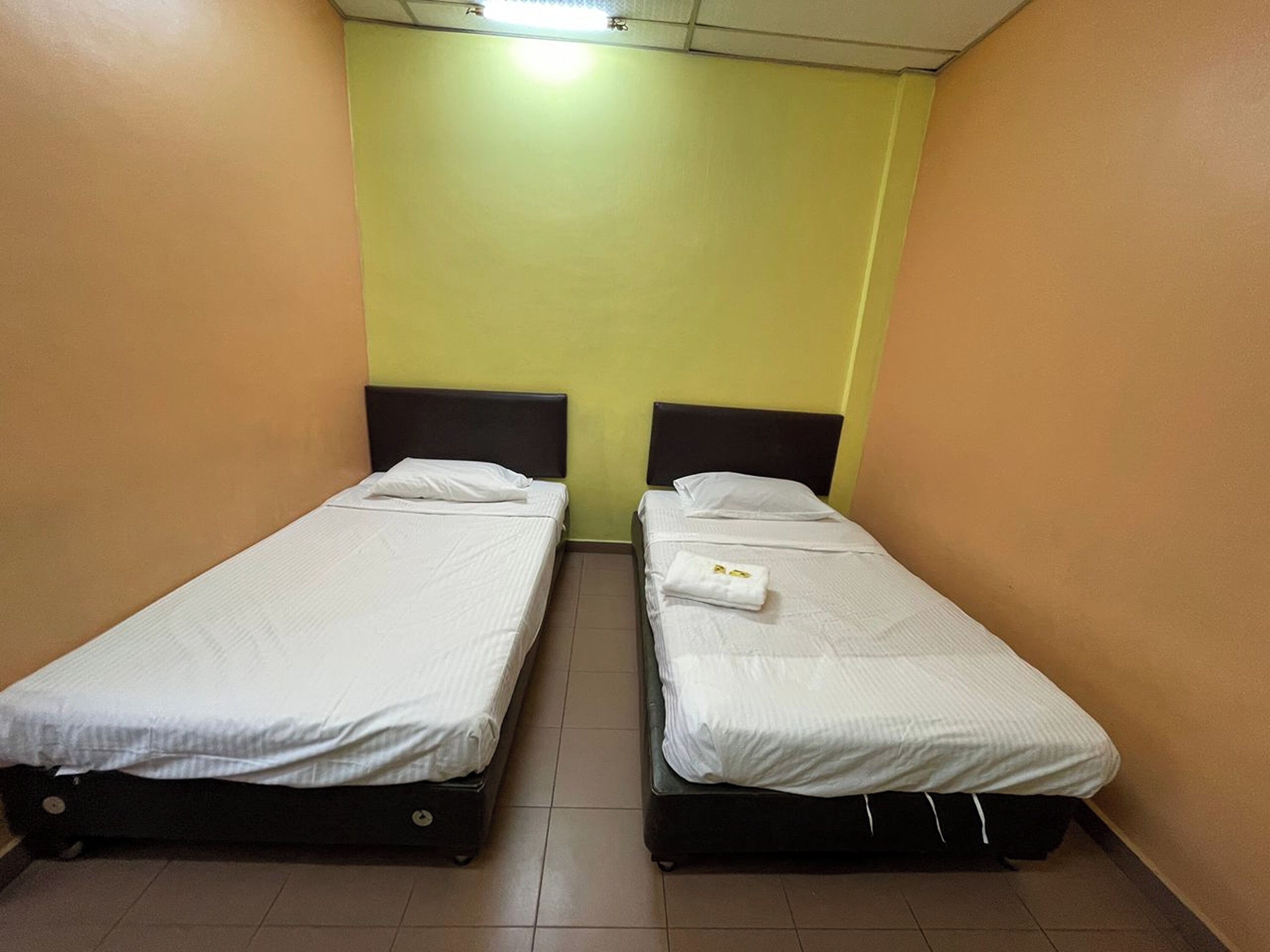 Two single beds with black frames in a room with yellow walls and a brown floor.