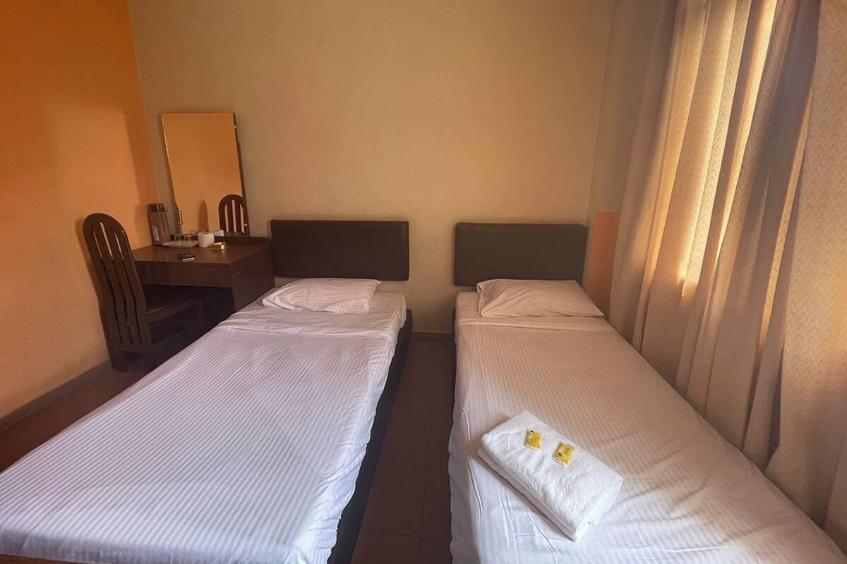 A hotel room with two single beds, a desk with a chair, a mirror, and a window with curtains.