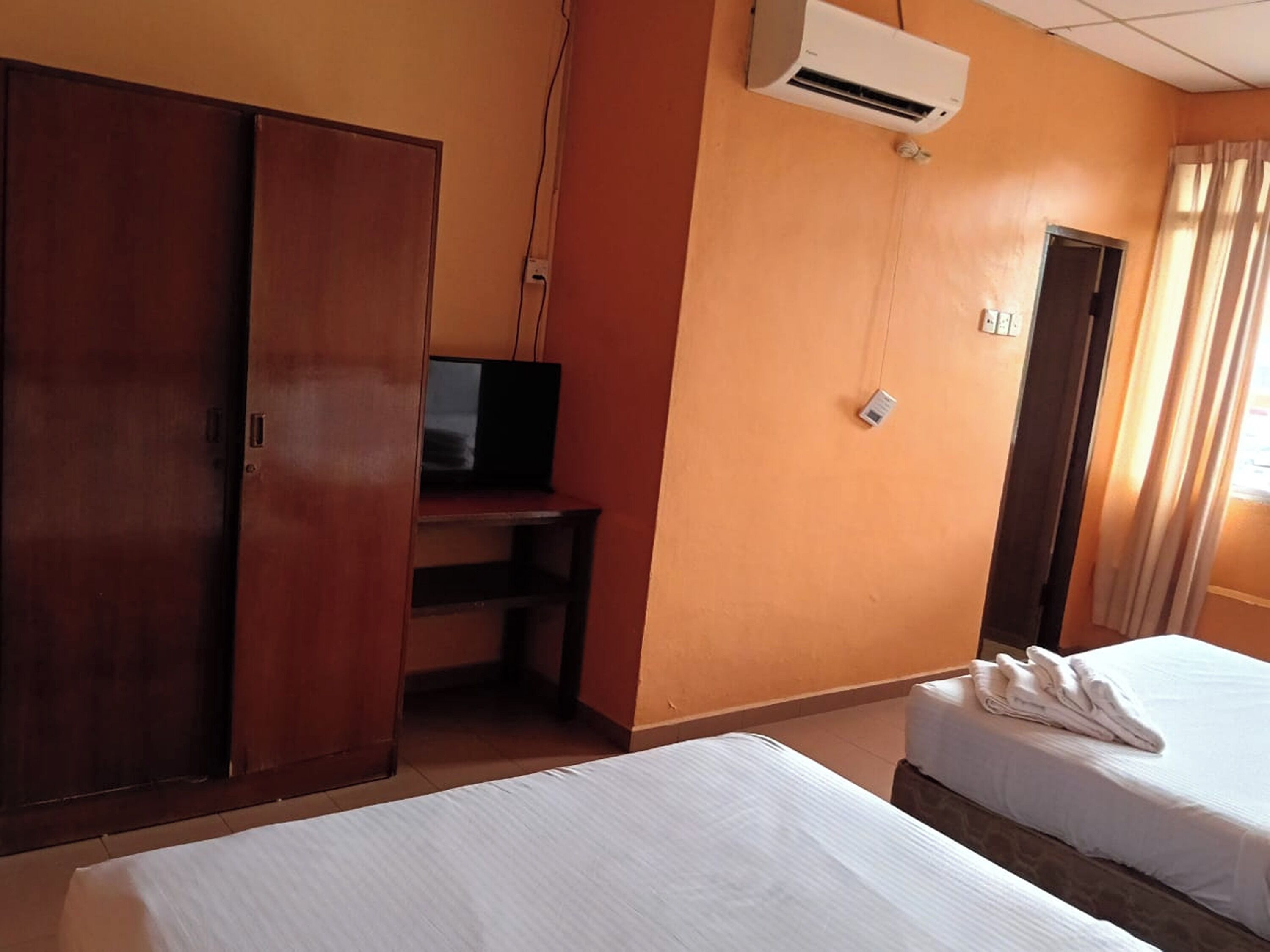 A hotel room with two beds, a TV, an air conditioner, and a wardrobe.