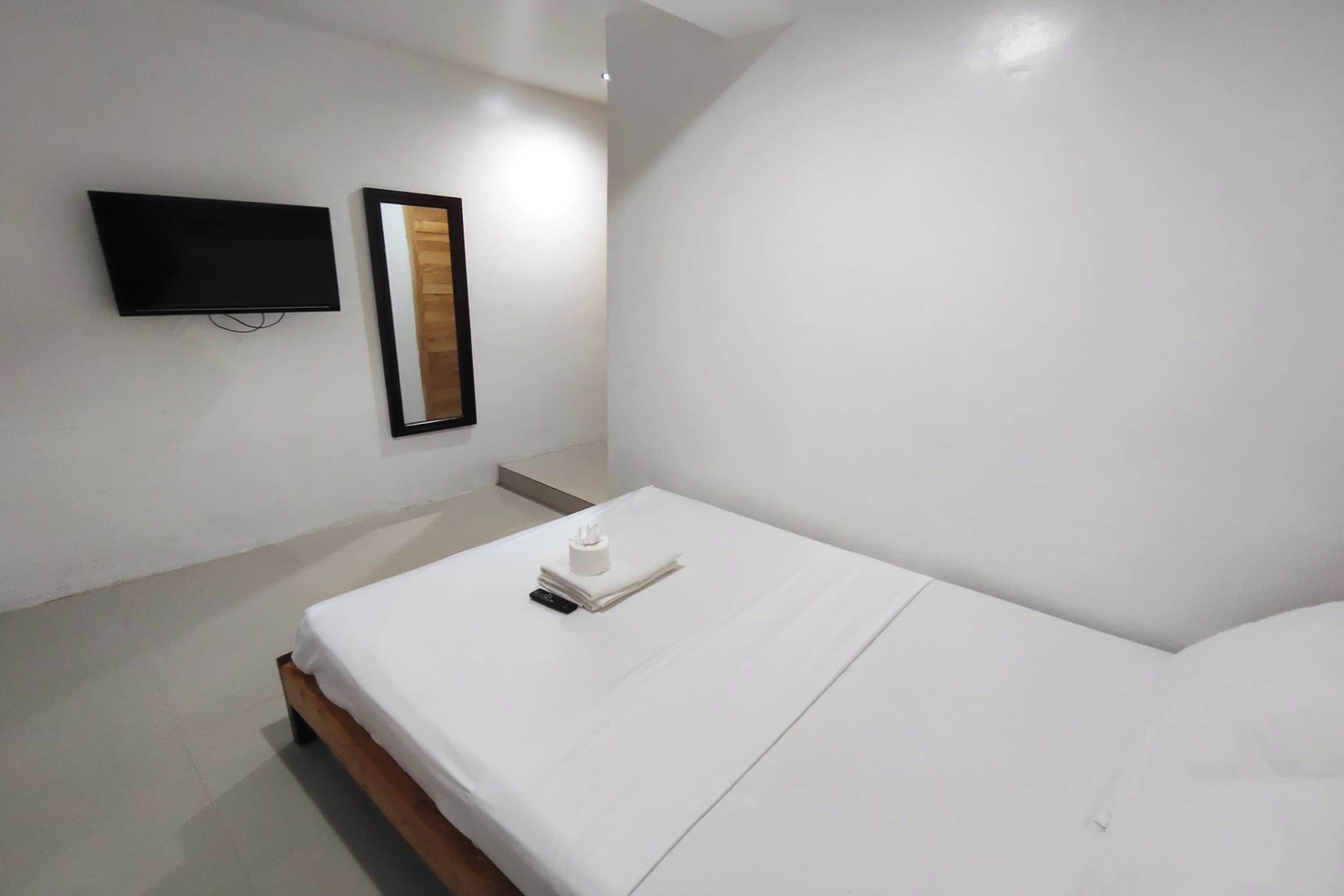 A hotel room with a bed, a TV mounted on the wall, and a mirror.