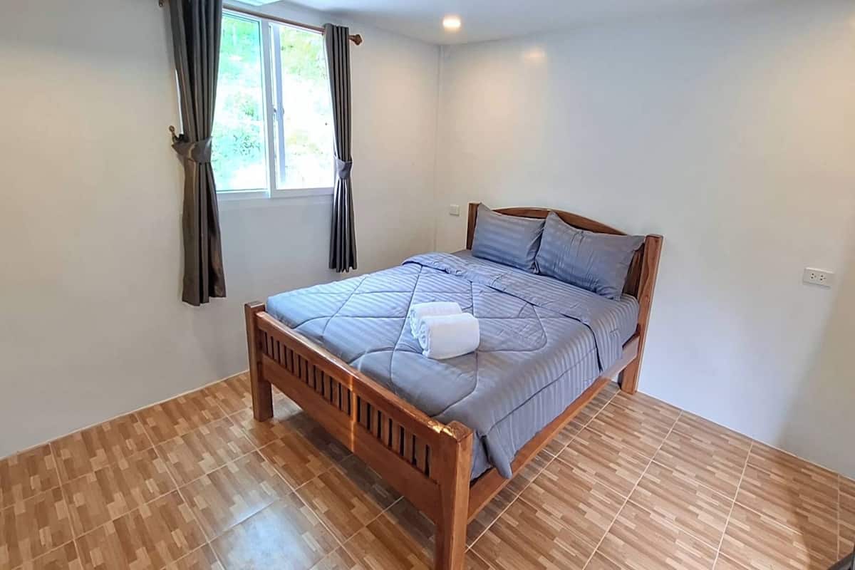 Ein Schlafzimmer mit einem hölzernen Bett, einem Fenster mit Vorhängen und einem Fliesenboden.