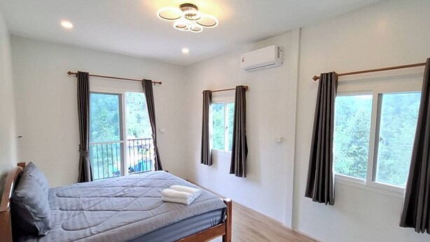 Un dormitorio con cama, dos ventanas con cortinas, un equipo de aire acondicionado y un balcón.