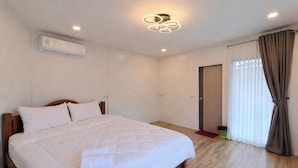 A bedroom with a bed, an air conditioning unit, a ceiling light fixture, a door, and a window with curtains. - Sawasdee@Ramrom (Ron Phibun)