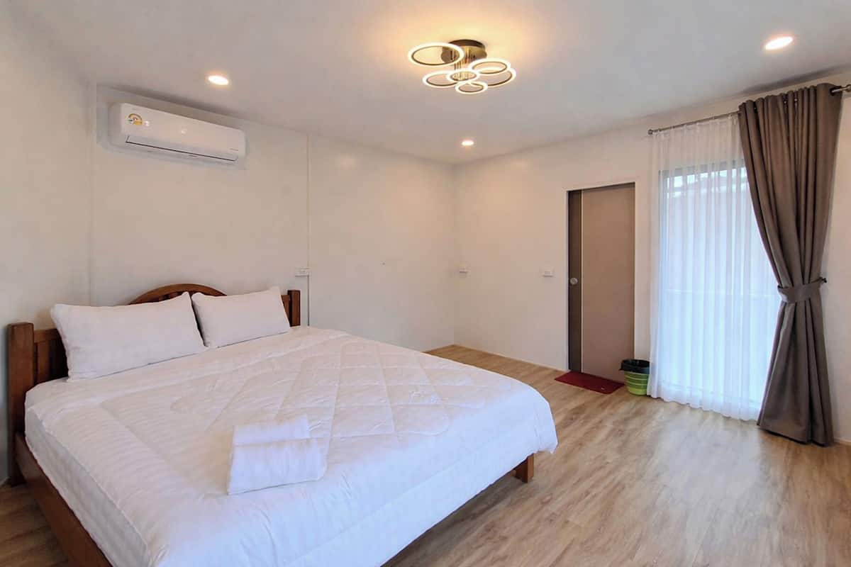 Ein Schlafzimmer mit einem Bett, einer Klimaanlage, einer Deckenleuchte, einer Tür und einem Fenster mit Vorhängen.