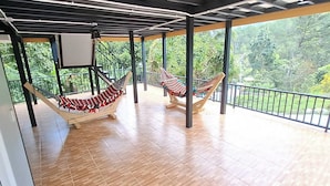 Un balcón techado con dos hamacas, piso de madera y vista a la vegetación.