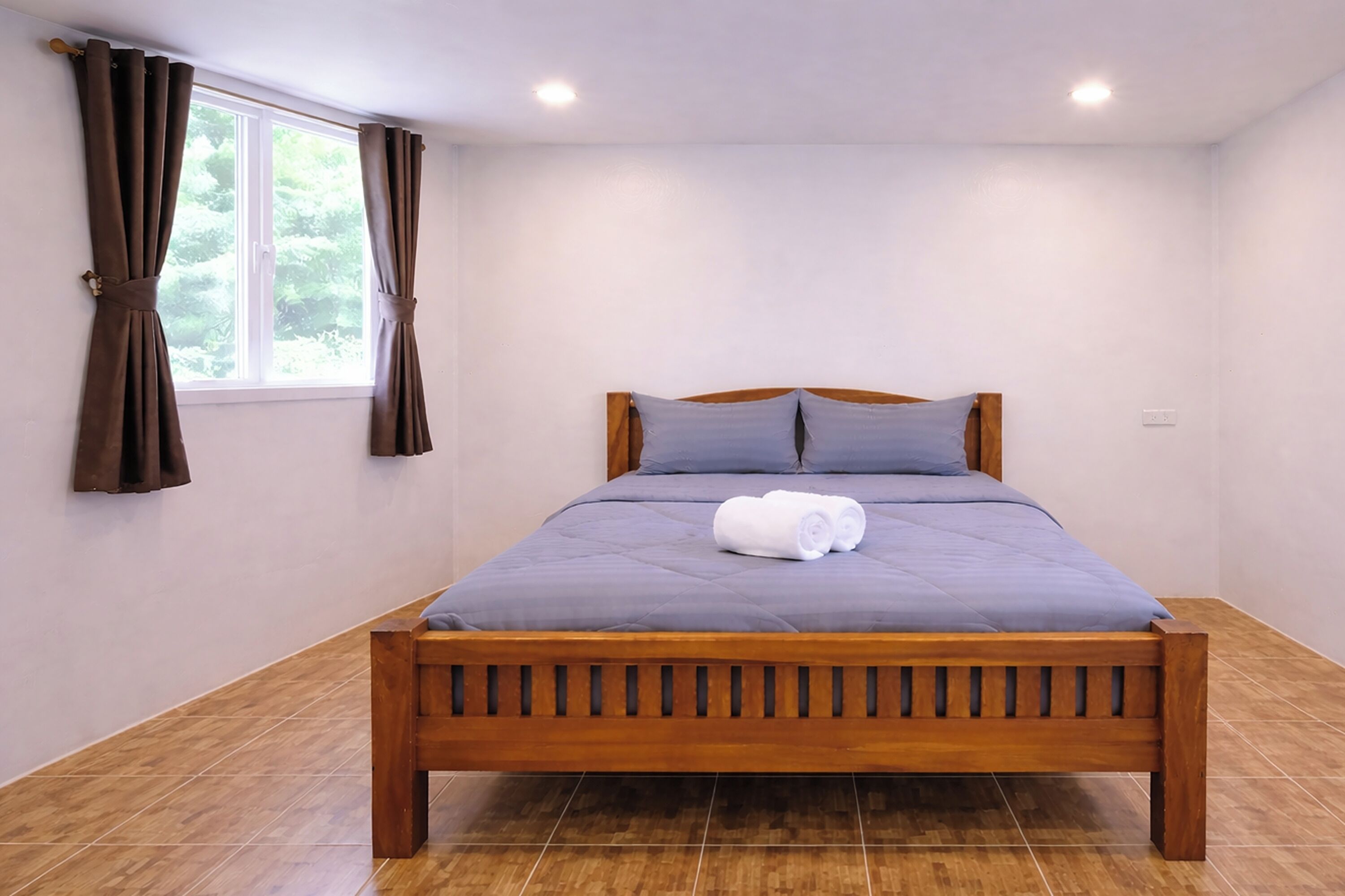 Una cama bien hecha con estructura de madera, una colcha gris y dos almohadas.
