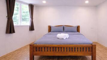 Una cama bien hecha con estructura de madera, una colcha gris y dos almohadas.