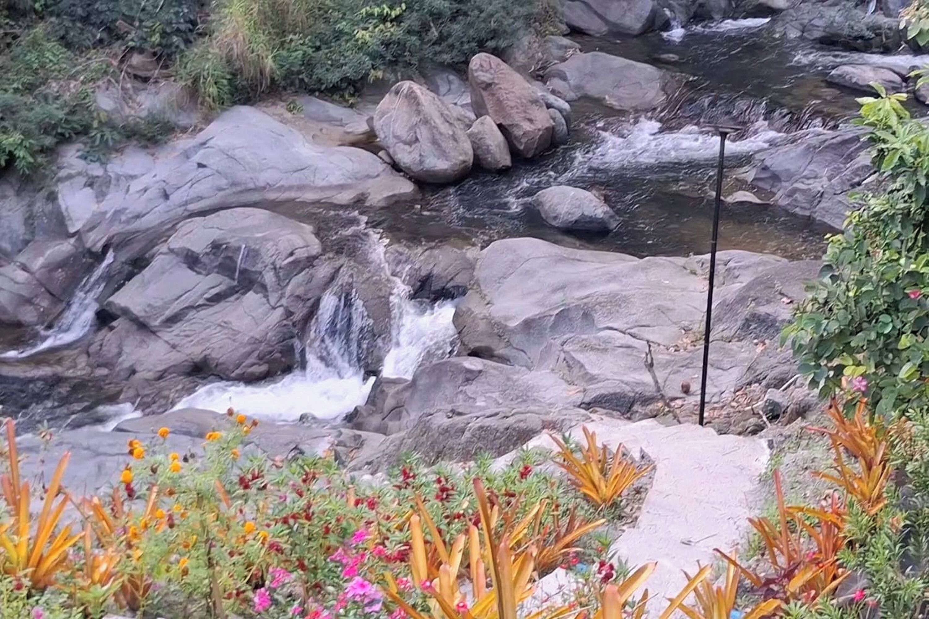 Un paysage naturel comprenant une cascade, de gros rochers et une végétation aux couleurs vives.