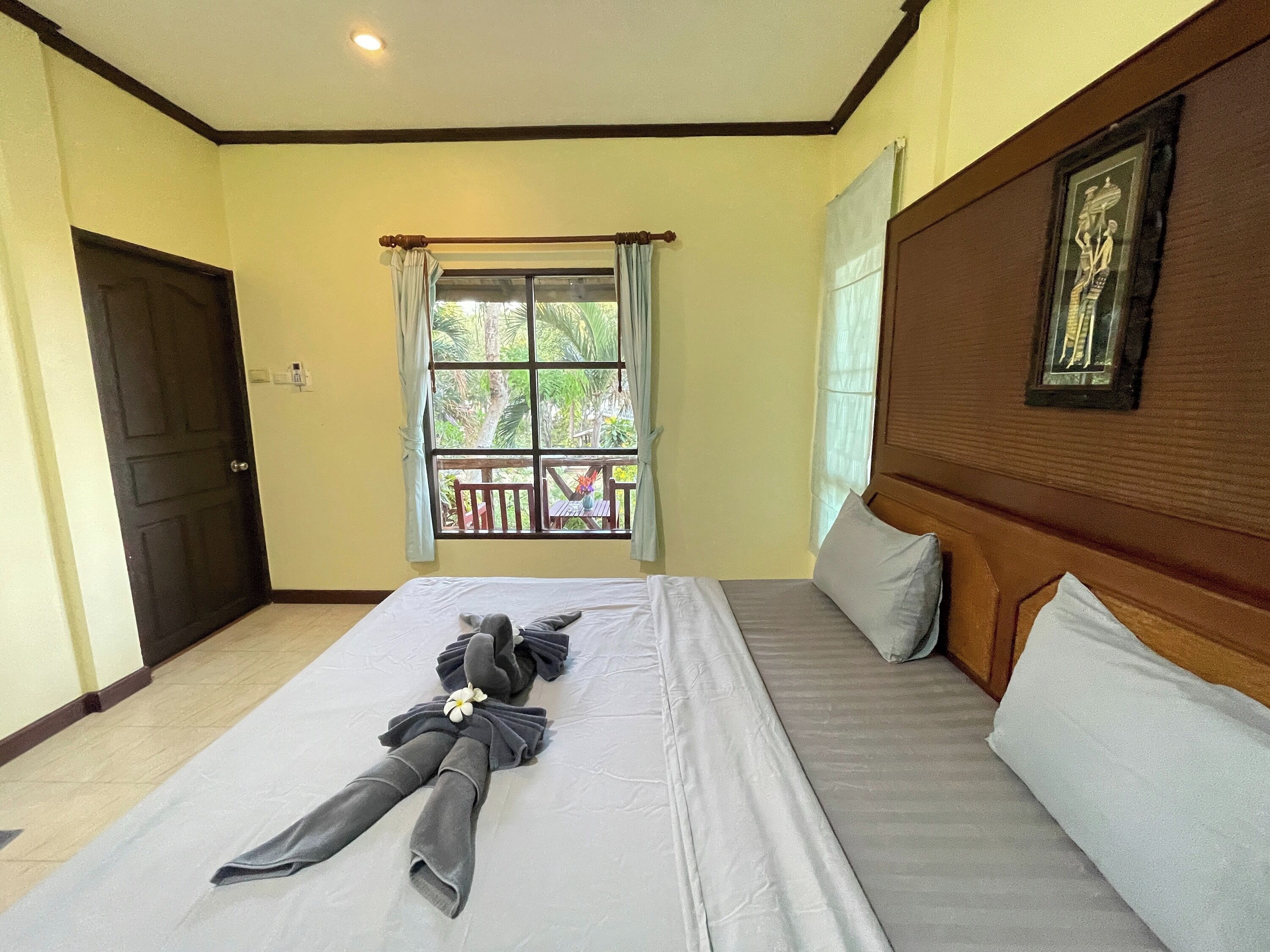 Una habitación de hotel con cama, ventana con cortinas, puerta y un cuadro en la pared.