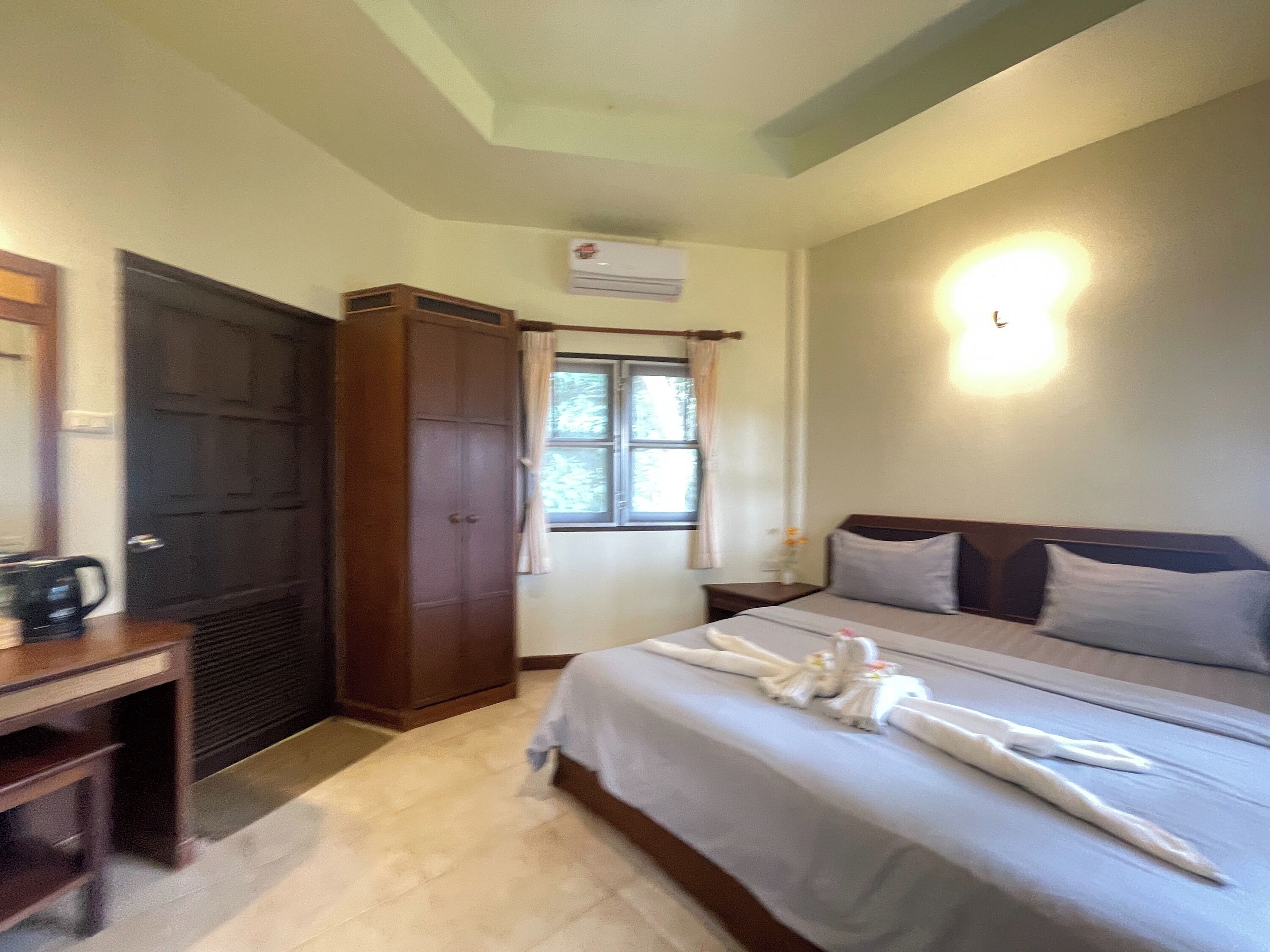 Una habitación de hotel con cama, escritorio, armario y ventana con cortinas.