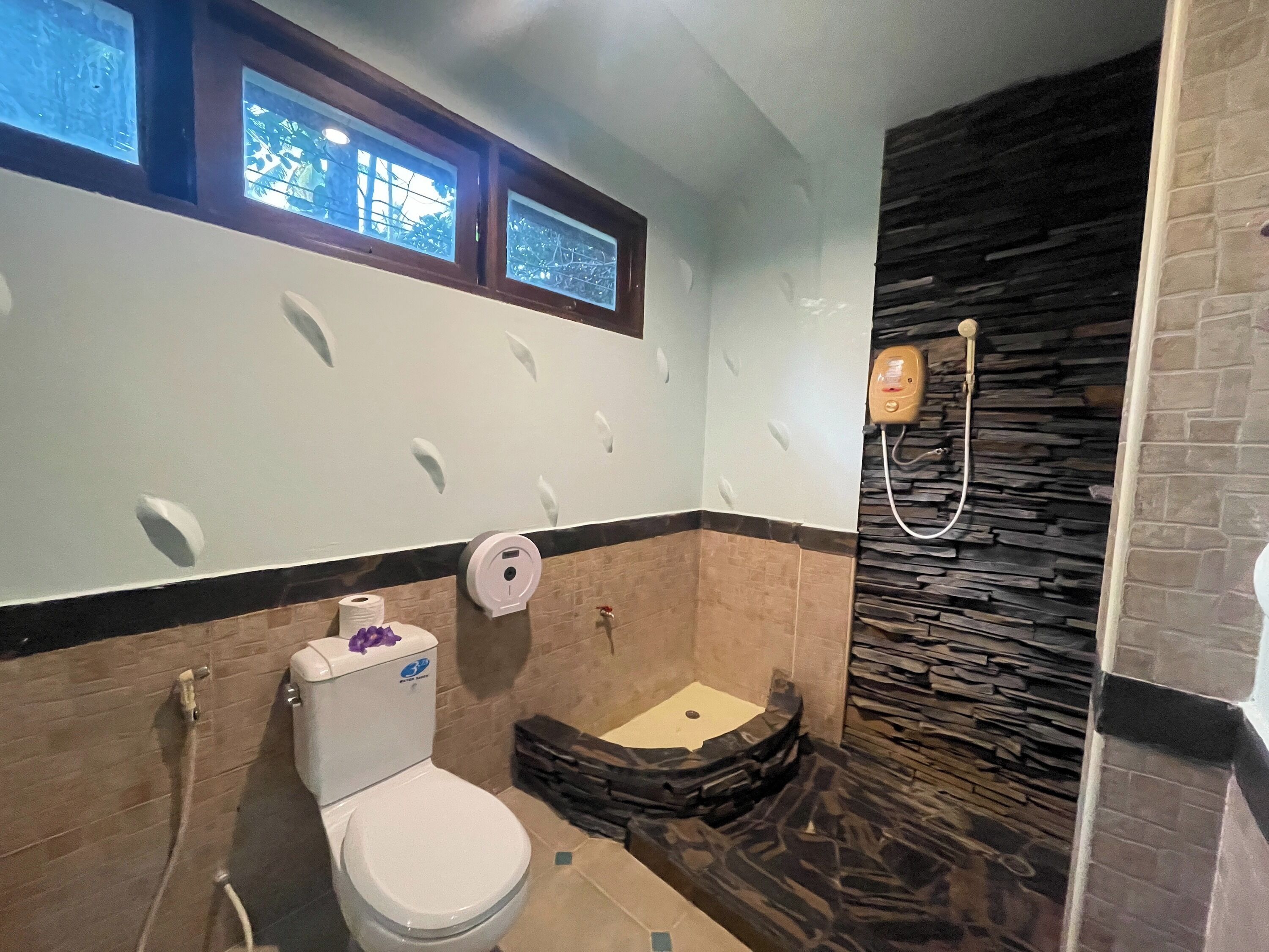A bathroom with a toilet, a shower, and a stone wall.