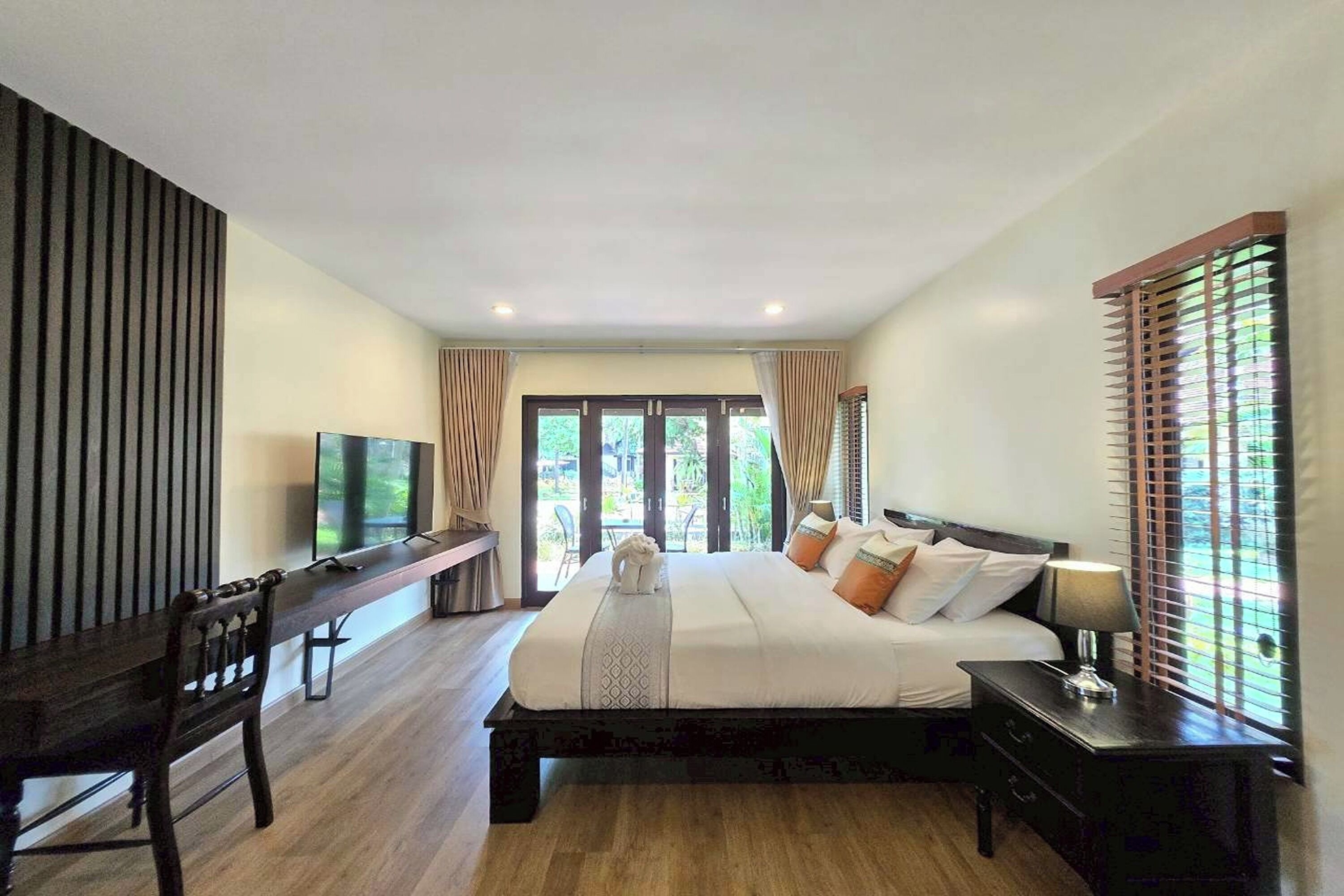 A bedroom with a bed, a desk, a TV, and a window with blinds.