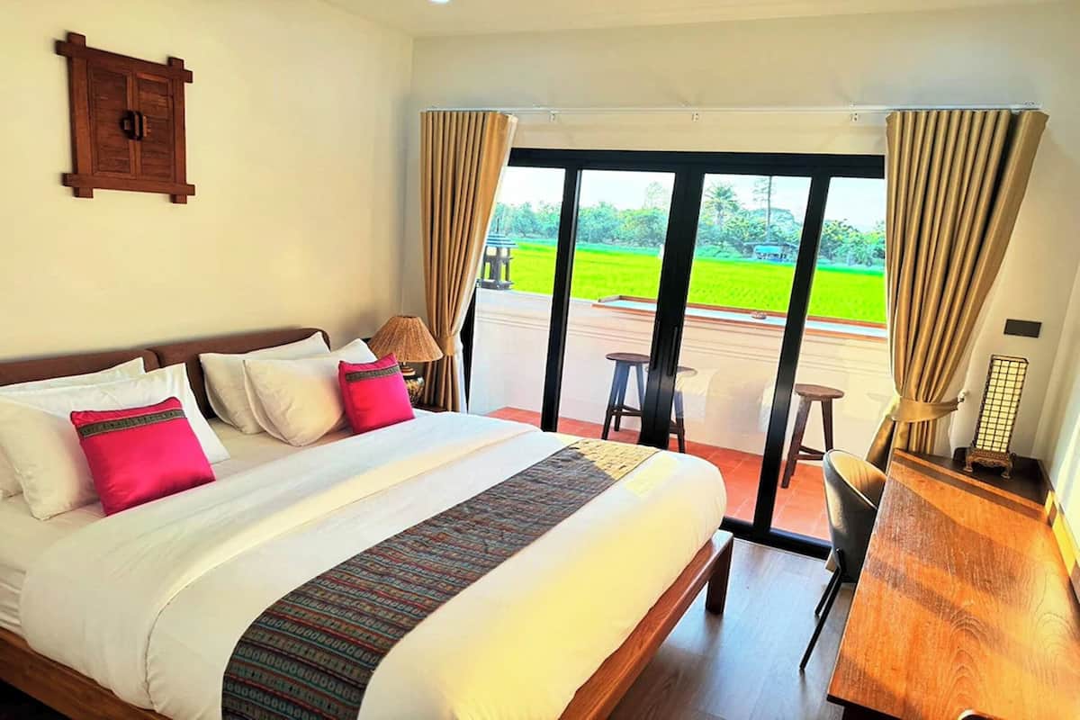 A hotel room with a large bed, a desk, and a view of a green landscape through the window.