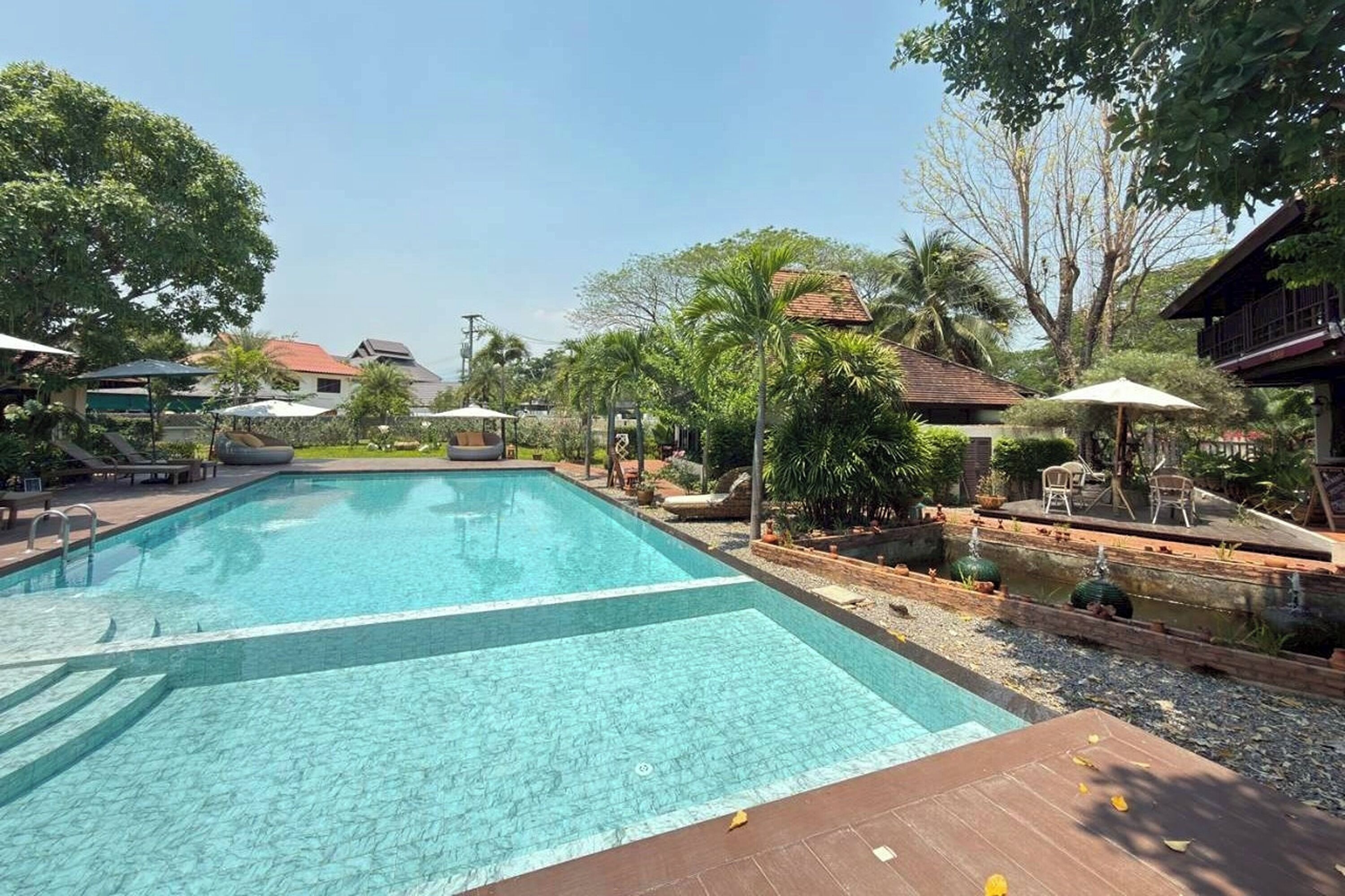 Ein rechteckiger Pool mit klarem Wasser, umgeben von Grünpflanzen und Gartenmöbeln.