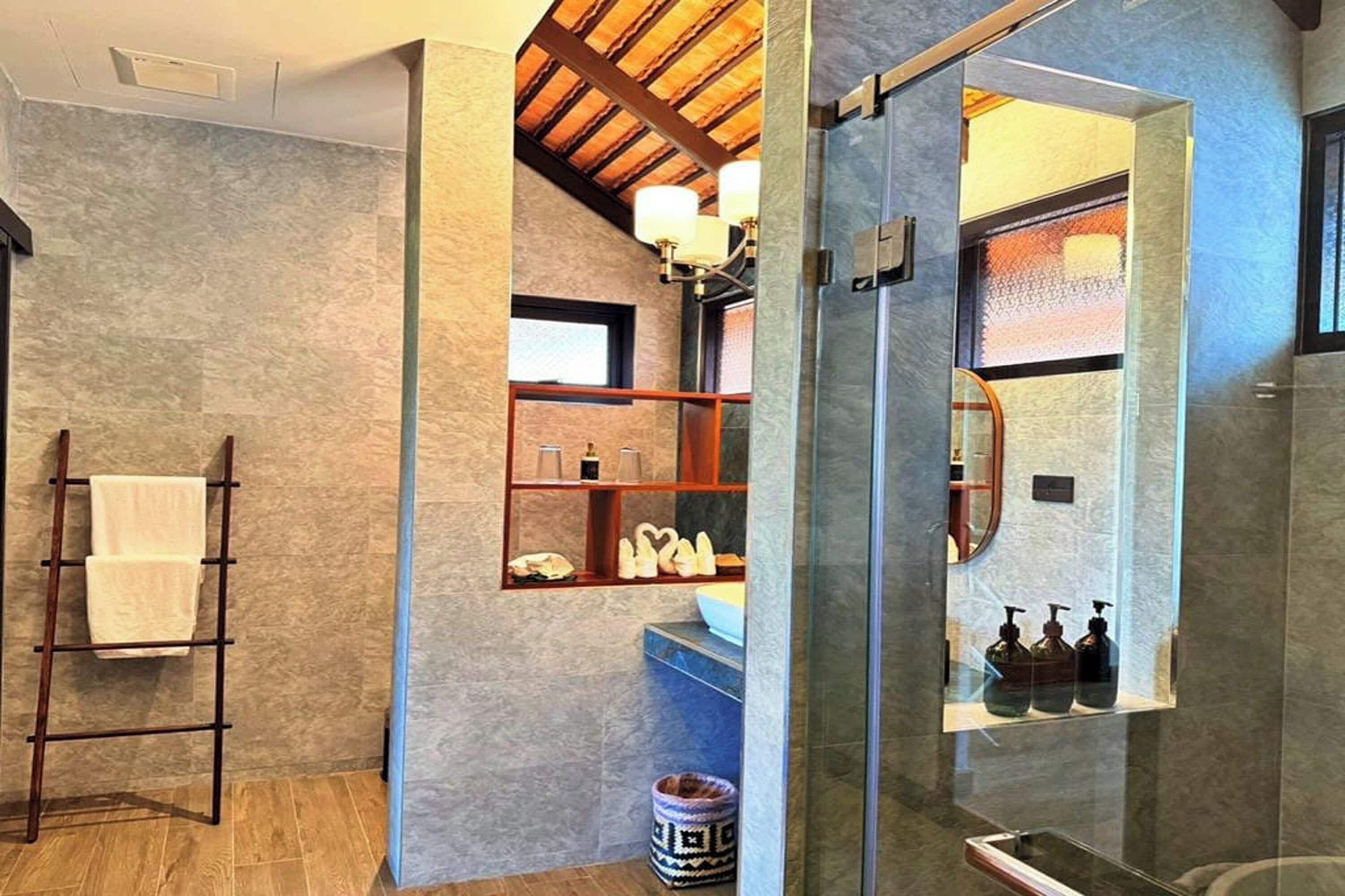 A modern bathroom with a wooden ladder, a shelf with toiletries, and a glass shower enclosure.