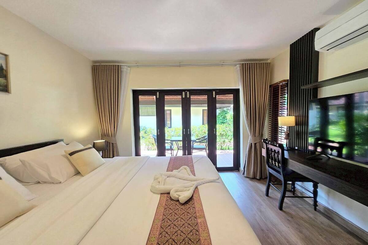 A hotel room with a bed, a TV, a desk, and a view of the outdoors through a sliding door.