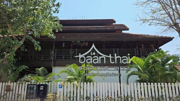 Un edificio con un letrero que dice 'baan thai BOUTIQUE VIETNA', rodeado por una cerca blanca de piquetes y palmeras.