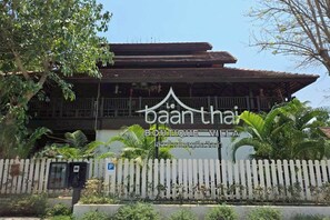 A building with a sign reading 'baan thai BOUTIQUE VIETNA,' surrounded by a white picket fence and palm trees.