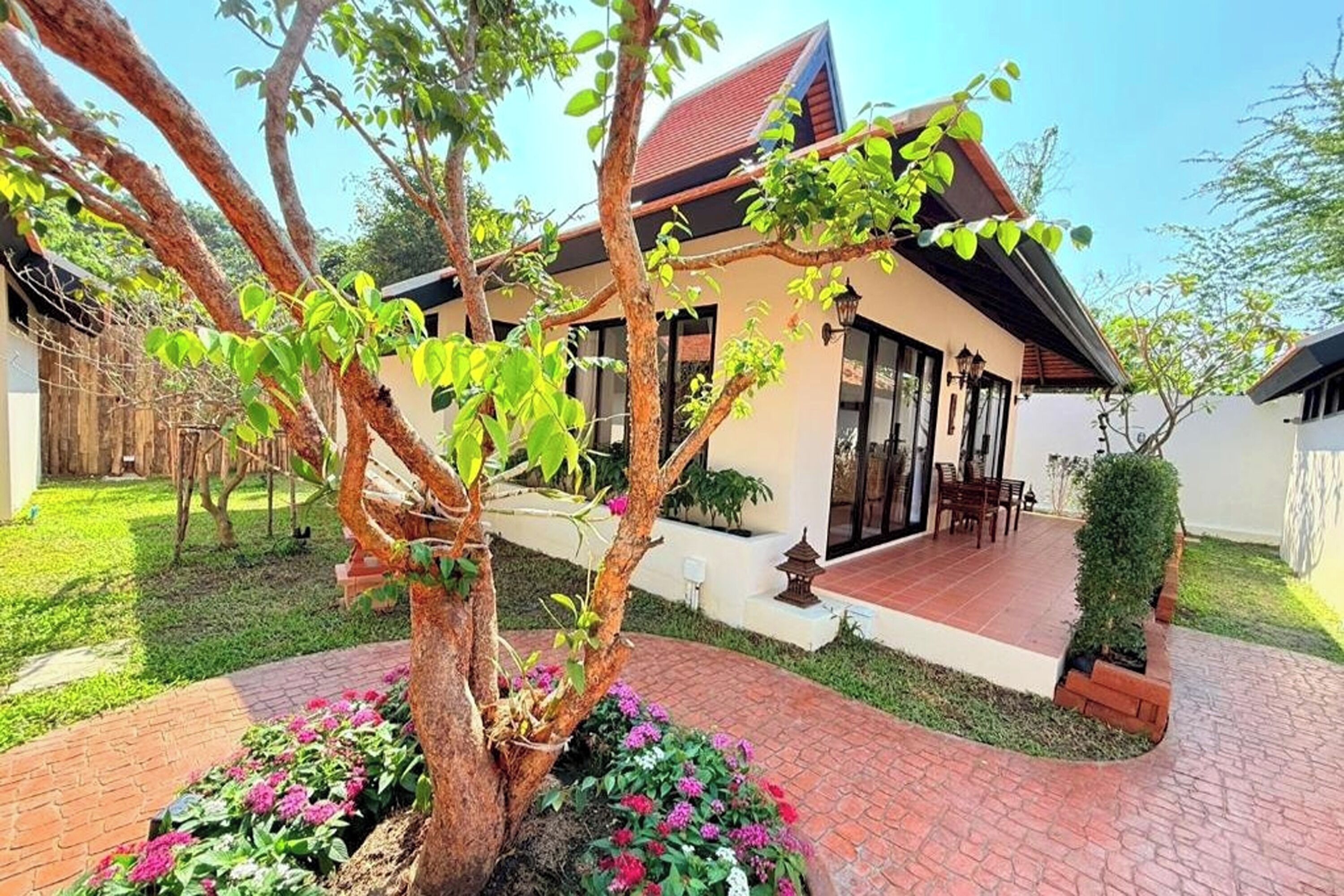 A house with a tiled patio, a tree in the center, and a small garden with flowers.