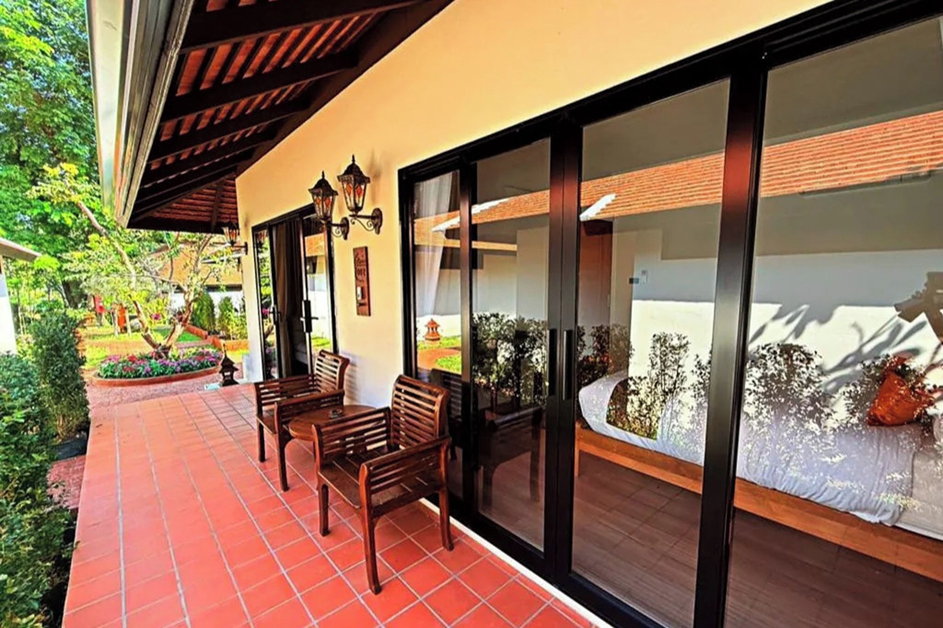 A patio with wooden furniture, a tiled floor, and a glass door leading to a garden.